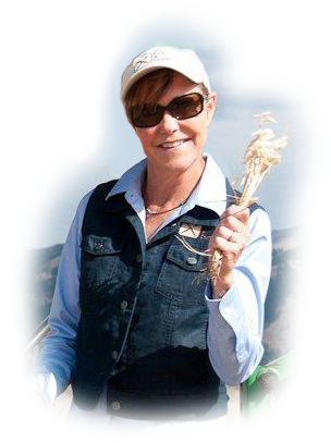 Smiling woman holding a feather outdoors with mountains in background.