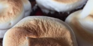 Toasted meringue cupcakes on a red surface.