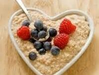 Heart-shaped bowl of oatmeal topped with fresh blueberries and raspberries.