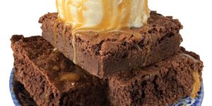 Brownies topped with vanilla ice cream on a decorative plate.