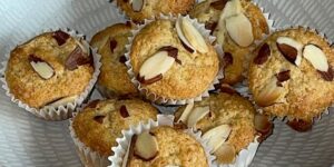 A bowl of freshly baked almond muffins topped with sliced almonds.