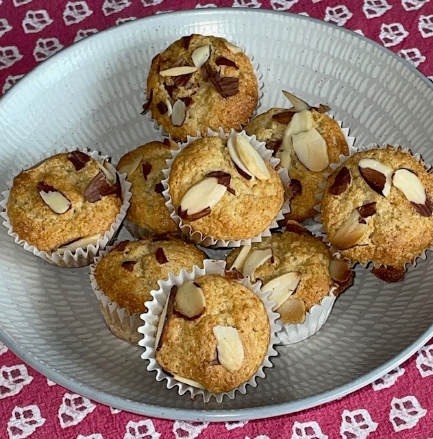 A bowl of freshly baked almond muffins topped with sliced almonds.