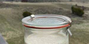 Jar of creamy yogurt with scenic mountain landscape in the background.