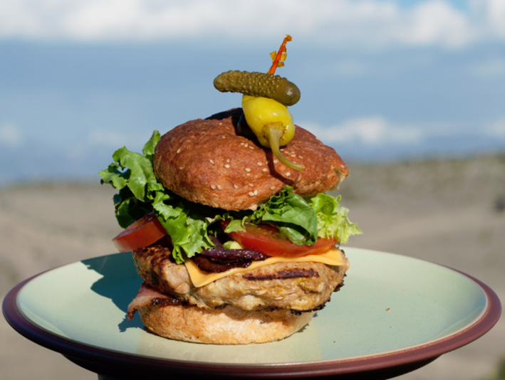A gourmet burger with lettuce, tomato, and a pickle on top.