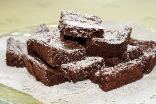 Stack of chocolate brownies dusted with powdered sugar on a glass plate.