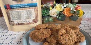 Homemade oatmeal raisin cookies on a plate beside a snack bag and decorative flowers.